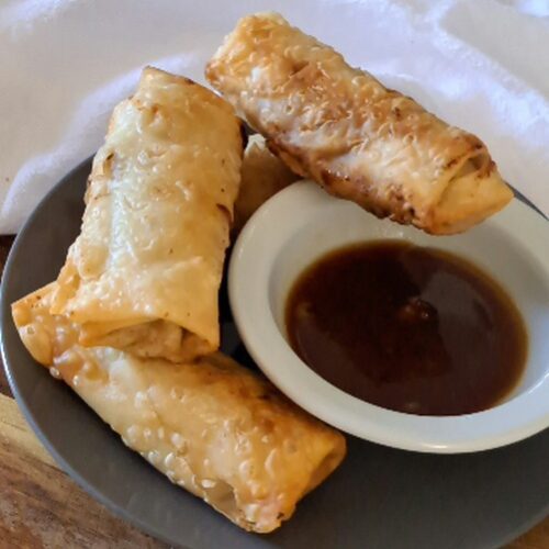 four crispy egg rolls piled around a small bowl of dipping sauce
